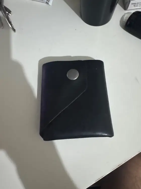 Seller's phone photo: a dark navy snap-closure card wallet on a white desk in harsh shadow